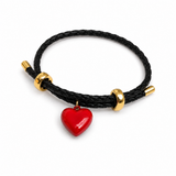 A black braided cord bracelet with gold-toned metal beads and a glossy red heart-shaped charm, shown on a clean white background.