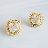 Elegant stud earrings featuring a stone encircled by small sparkling crystals, all set in a polished gold frame. The cushion-cut center gem catches the light beautifully, creating a timeless and sophisticated look.