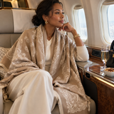 Model wearing Ellison+Young Luxe Bandana Paisley Shawl Scarf in Camel Ivory draped over her shoulders in an airplane cabin