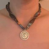 Elegant scarf necklace featuring a bold medallion pendant and luxe printed fabric intertwined with a chain, combining statement style with wearable versatility.