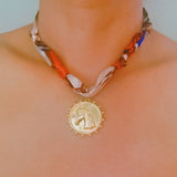 Elegant scarf necklace featuring a bold medallion pendant and luxe printed fabric intertwined with a chain, combining statement style with wearable versatility.