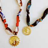 Elegant scarf necklace featuring a bold medallion pendant and luxe printed fabric intertwined with a chain, combining statement style with wearable versatility.