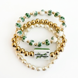 Set of three beaded bracelets with gold, green, and white beads on a white background