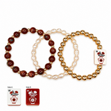 Three beaded stretch bracelets arranged on a white background, with two bracelets in dark reddish-brown and one in cream and gold. Each bracelet has a square floral charm.
