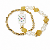 A gold beaded bracelet with white baroque pearls, translucent yellow stone beads, and a square white enamel tile charm featuring a painted flower and the number 4, shown on a white background.