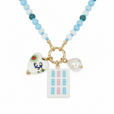 A beaded necklace with light blue, white, and teal beads, featuring gold-tone hardware and three charms: a white heart with colorful floral and dragon details, a white pearl bead, and a white rectangular tile charm printed with pink and blue numbers resembling mahjong tiles.