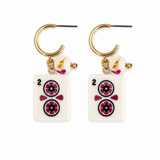A pair of gold hoop earrings with dangling rectangular white tiles printed like playing cards, featuring black numbers and circular floral motifs in pink, black, and white, with small gold and pink charms below.