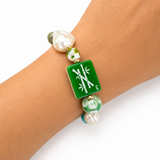 Bracelet with green square charm and pearls on a wrist against a white background
