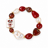 A beaded stretch bracelet featuring red and dark brown agate-like beads, white baroque pearls, a square white tile charm with a red floral vase motif, and gold-tone spacer rings, shown on a plain white background.