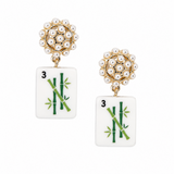 A pair of gold and white drop earrings featuring a cluster of faux pearls at the top and a rectangular white tile below printed with green bamboo and the number 3, set against a plain white background.