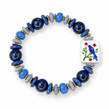 A beaded stretch bracelet featuring navy blue and light blue beads, gold spacer rings, and a square white tile charm decorated with a blue bird and red flowers, shown on a plain white background.