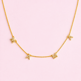 Gold necklace with butterfly pendants on a pink background