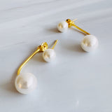 A pair of modern pearl earrings featuring a sleek gold-tone bar connecting two lustrous pearls—one smaller and one larger—for a minimalist yet elegant look. These dual pearl drop earrings combine classic sophistication with a modern silhouette.