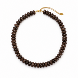 A dark brown beaded necklace made of small, polished disc-like beads, featuring a gold-tone chain extender clasp with a small tag, displayed on a clean white background.