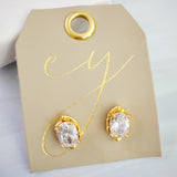 Chic stud earrings featuring a fluid, molten metal frame wrapped around a sparkling oval-cut crystal, offering a refined mix of organic shape and radiant shine.