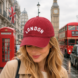 Woman wearing a red 'London' cap with iconic London sights in the background.