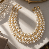 Noble Pearl 3-Piece Necklace Set laid flat on a marble vanity in soft sunlight, showing three graduated pearl strands and gold extender chains