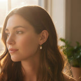 A pair of elegant drop earrings featuring organic-shaped baroque pearls with gold-tone vine-like prong detailing, suspended from sleek curved gold hooks, displayed against a dark textured background.