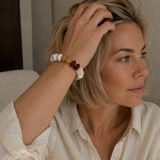 A woman with blonde hair wearing a beaded bracelet on her wrist, shown in a close-up profile view. The bracelet features white, amber, and dark brown beads.