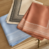 Three folded napkins in blue, beige, and brown with intricate patterns on a wooden surface.