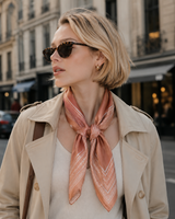 Woman wearing a beige trench coat and sunglasses with a pink scarf in an urban setting