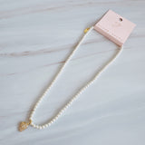 Refined pearl necklace featuring a small gold heart pendant adorned with sparkling crystals. The minimalist yet elegant design offers a timeless touch perfect for layering or wearing on its own.