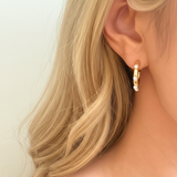 Polished gold hoop earrings adorned with small white pearls evenly spaced around the hoop. The design combines modern structure with classic pearl accents for a refined yet trendy look.