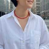 Close-up of a bold red beaded necklace featuring uniformly round, glossy beads strung together in a classic strand, creating a vibrant and timeless accessory.