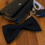 Black bow tie and quilted black wallet on a wooden surface