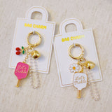 Playful bag charm featuring two pink pickleball paddles—one with cherries and one with “Let’s Pickle” text—accented with a cherry charm and gold-tone details for a fruity, sporty twist.