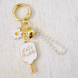 Decorative bag charm featuring a pickleball paddle- with “Let’s Pickle” text—plus a daisy flower and gold-tone accents, perfect for adding a playful touch to any bag.