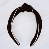 Structured preppy headband featuring a contrasting piped border detail, adding a polished and classic touch to any hairstyle.