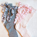 Set of two socks featuring plaid patterns with ruffle bow accents, combining classic charm with playful, feminine details.