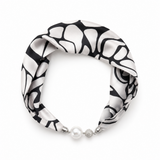 A black and white abstract patterned silk scarf styled as a headband with a pearl and silver bead closure, shown on a plain white background.