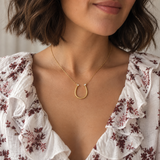 Model wearing the dainty gold Sculpted U Pendant Necklace with a ruffled white floral blouse