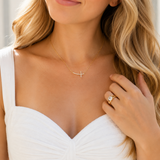 Woman wearing a gold necklace with a cross pendant and a white dress.