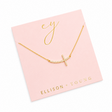 Gold necklace with a diamond-studded cross pendant packaged on pink Ellison + Young logo brand card on a white background