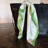 Green and white patterned scarf draped over a black handbag on a marble surface