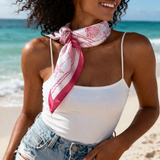 Woman on a beach wearing a white top and denim shorts with a pink and white scarf.