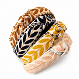 Four woven fabric headbands with leaf patterns in brown, navy, mustard yellow, and blush pink, arranged in a stack on a white background.