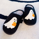 Black cozy slippers featuring a white ghost with a pumpkin detail, offering a playful and spooky seasonal touch.