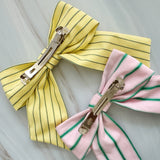 Striped ribbon bow hair clips in pastel pink with green stripes and soft yellow with blue stripes. The Striped Ribbon Bow Hair Clip – Classic Preppy Style adds a charming, polished accent to any hairstyle, blending playful color with timeless sophistication.