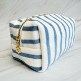 Blue and white striped pouch with a gold zipper on a light wooden surface
