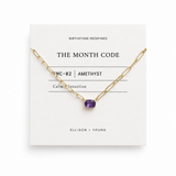 Gold necklace with a purple gemstone on a white card displaying 'The Month Code' branding.