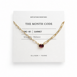 Gold necklace with a red gemstone on a white card with 'The Month Code' branding.