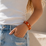 Person wearing a white top and blue jeans with a red bracelet on a neutral background