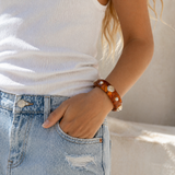 Person wearing a white sleeveless top and light blue jeans with a brown bracelet on a neutral background