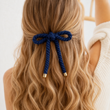 Navy blue hair bow with gold accents in wavy blonde hair against a neutral background