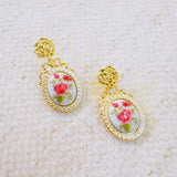 Gold-tone vintage-style drop earrings featuring an oval cameo with delicate pink rose floral design and ornate top stud
