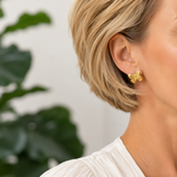 Close-up of a person wearing gold earrings with a blurred green plant background